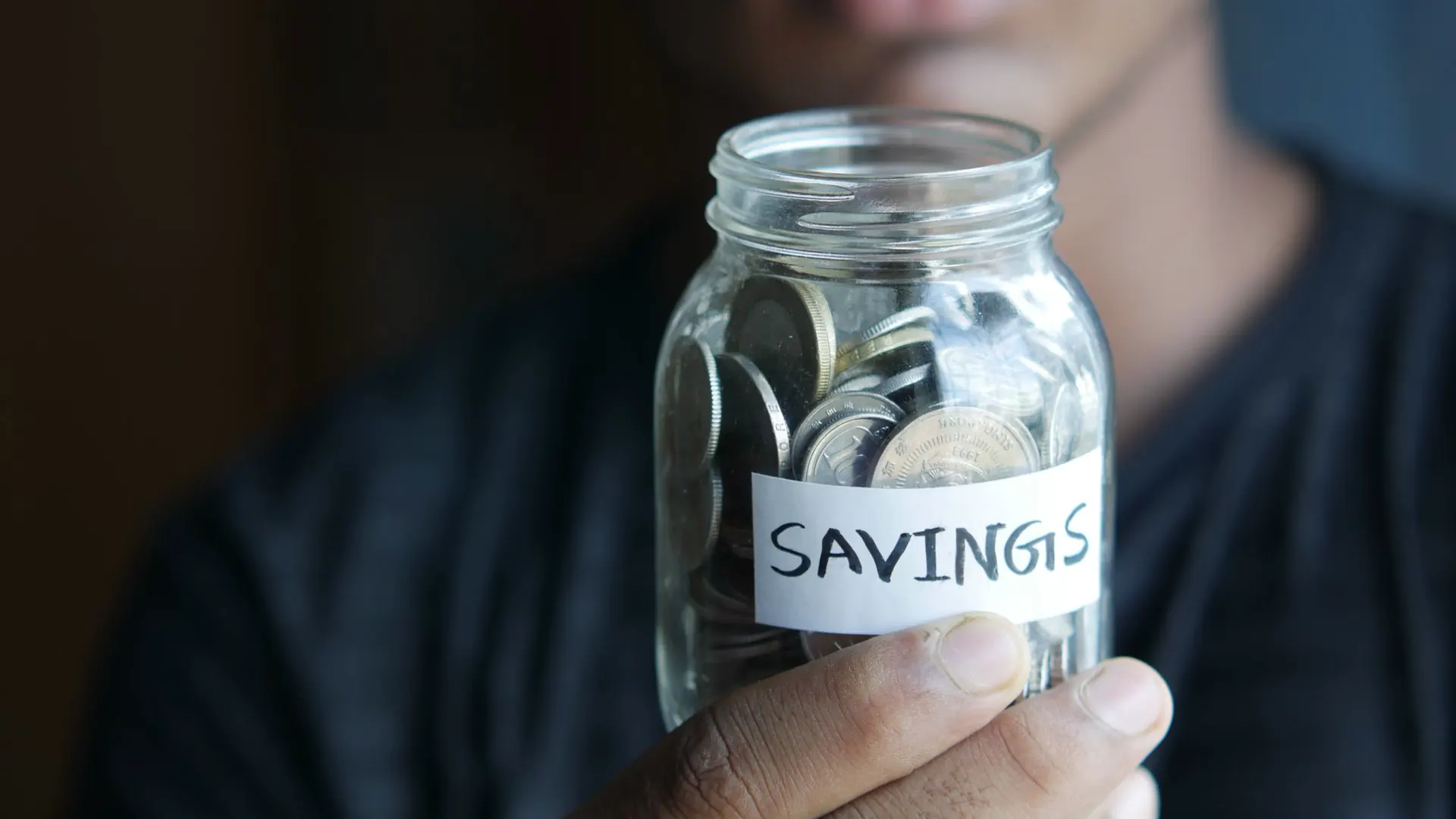 A student holds up a glass jar of coins labelled savings